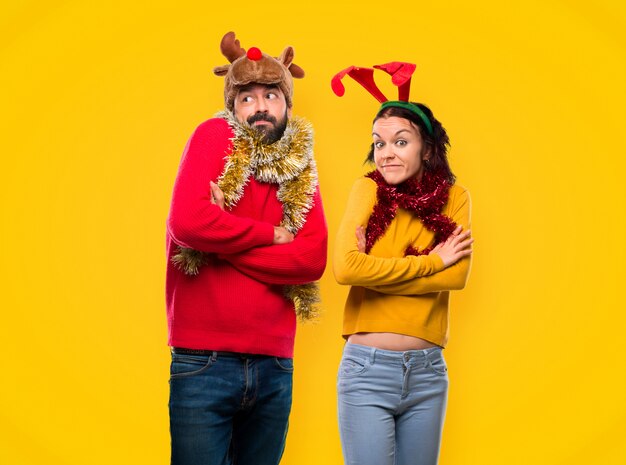 Pareja vestida para las vacaciones de Navidad haciendo un gesto sin importancia mientras levanta el