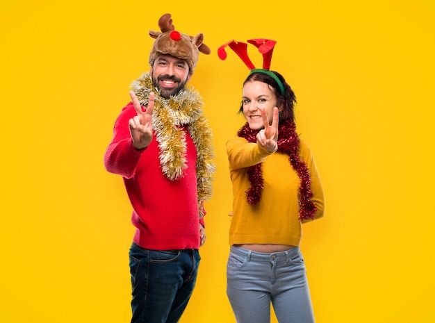 Pareja vestida para las vacaciones de Navidad sonriendo y mostrando el signo de la victoria