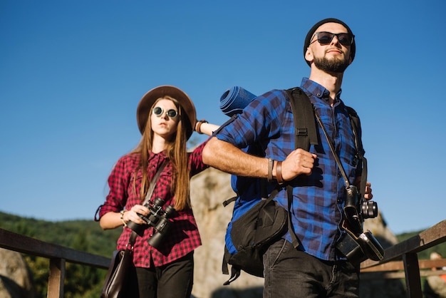 Una pareja viajando por las montañas vistiendo ropa hipster con mochila, cámara vintage y binoculares