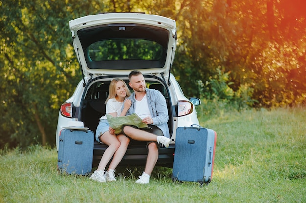 Pareja de viajero sentado en el hatchback del coche cerca de la carretera durante las vacaciones.