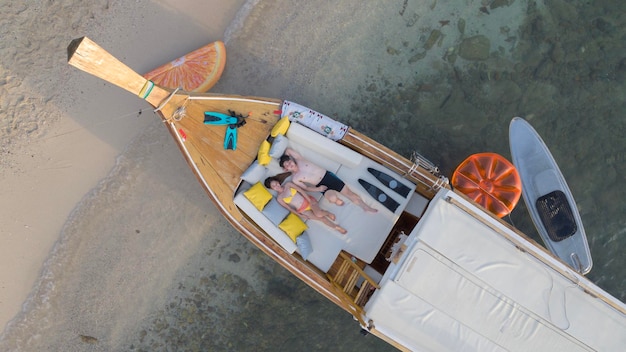 Una pareja de viajeros asiáticos sentados y viendo la puesta de sol juntos en la playa con fondo de barco de cola larga