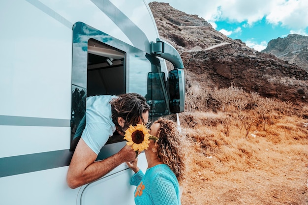 Foto pareja de viajeros besándose y amándose en el destino hombre dentro de una autocaravana y una mujer afuera en una relación felicidad y estilo de vida del viajero vehículo rv moderno para viajes por carretera vacaciones fuera de la red