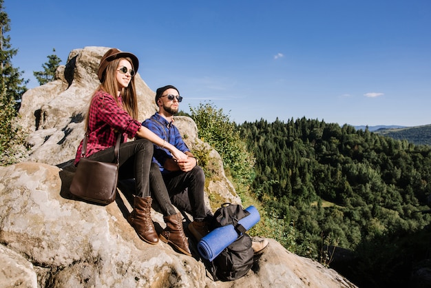 Una pareja de viajeros descansando en la cima de las montañas rocosas y mirando el paisaje