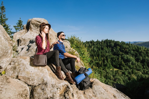 Una pareja de viajeros descansando en la cima de las montañas rocosas y mirando el paisaje