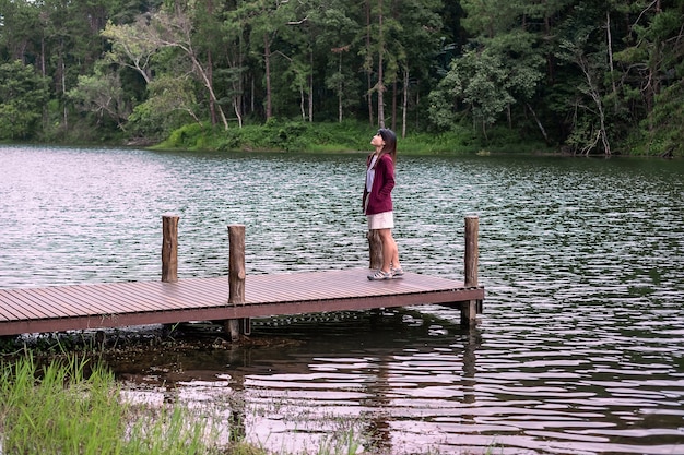 Pareja de viajeros felices de pie en un muelle con un fondo de río y bosque