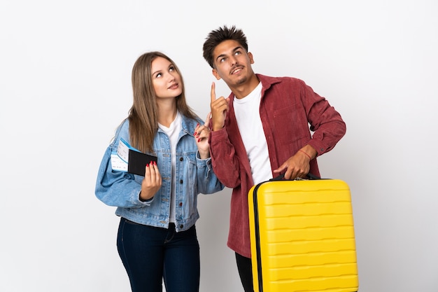 Pareja de viajeros sosteniendo una maleta en azul apuntando con el dedo índice una gran idea