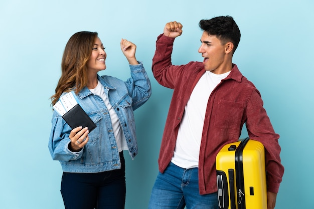 Pareja de viajeros sosteniendo una maleta en azul celebrando una victoria en la posición ganadora