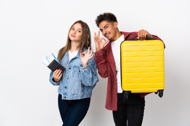 Pareja de viajeros sosteniendo una maleta en azul mostrando un signo de ok con los dedos