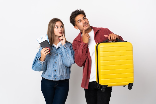 Pareja de viajeros sosteniendo una maleta en azul pensando en una idea mientras mira hacia arriba