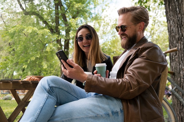 Pareja vistiendo chaquetas de cuero sintético tomando selfie al aire libre mientras toma un café