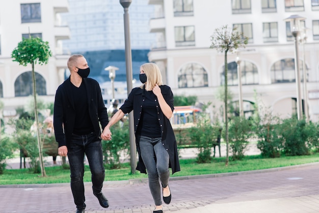 Pareja vistiendo máscaras protectoras de moda, caminando en la calle vacía de la ciudad durante la cuarentena