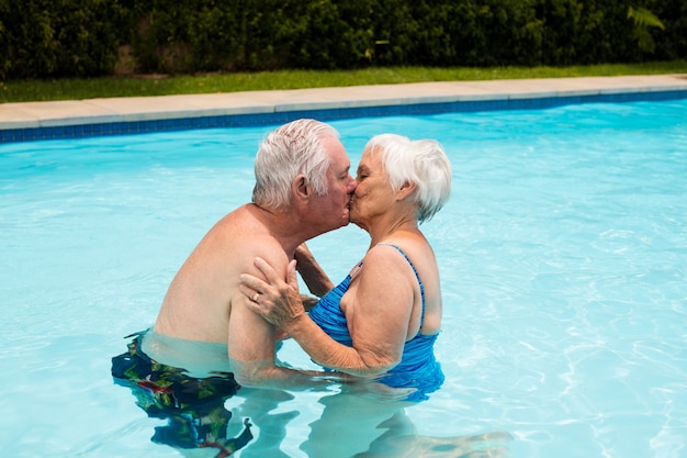 Las parejas ancianas besándose en la piscina en un día soleado