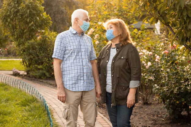 Las parejas ancianas caminando afuera en la naturaleza con máscaras médicas