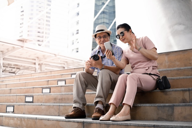 Las parejas asiáticas mayores se sientan en las escaleras mientras viajan y se divierten haciendo videollamadas.