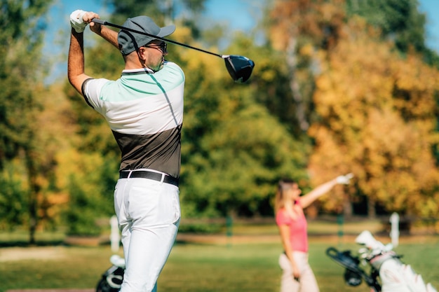 Parejas de golf Joven dando el primer golpe a su compañero siguiendo la pelota