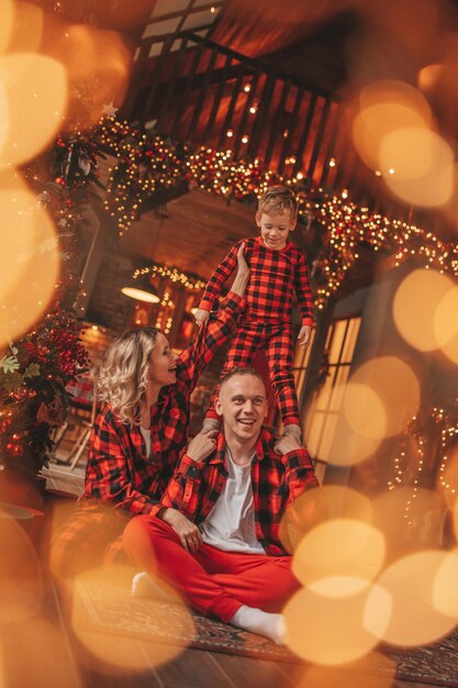 Foto parentes ativos sorridente com filho pequeno em pijama a quadros vermelhos esperando o papai noel dentro de casa