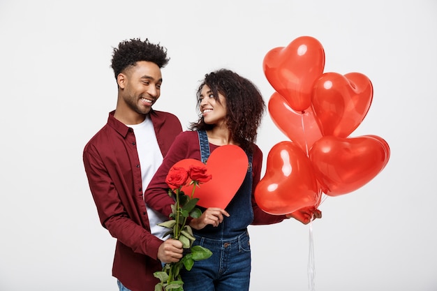 Pares afro-americanos atrativos novos em datar com rosa, coração e balão do vermelho.