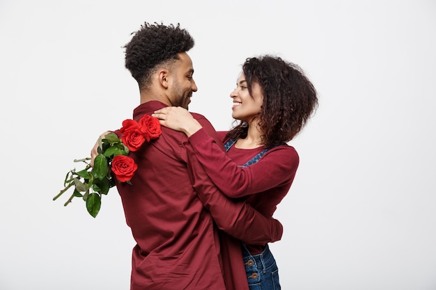 Pares afroamericanos jovenes que se abrazan y que sostienen la rosa roja romántica.