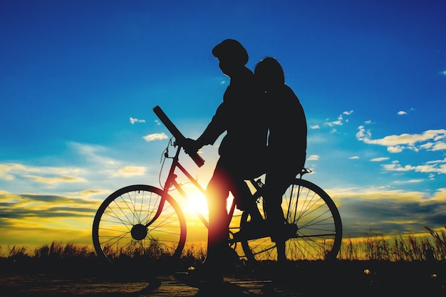 Pares e bicicleta das silhuetas no céu do por do sol, conceito dos pares.