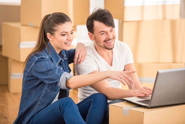 Pares felices jovenes que buscan para los apartamentos con la computadora portátil.