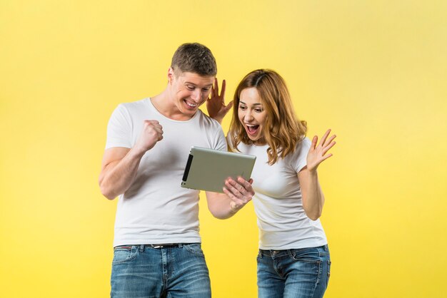 Foto pares jovenes emocionados que miran la tableta digital contra el contexto amarillo