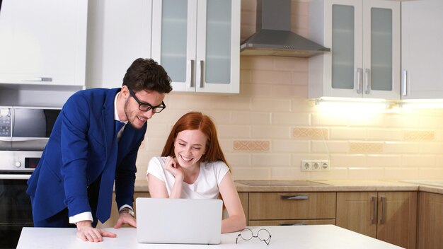 Pares jovenes del negocio que hablan y que usan la computadora portátil en cocina en casa.