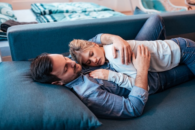 Pares jovenes en la ropa casual que duerme junto en el sofá azul en casa.