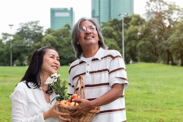 Pares mayores asiáticos con felicidad de la forma de vida de la cesta de fruta en parque.