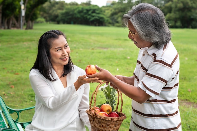 Pares mayores asiáticos con felicidad de la forma de vida de la cesta de fruta en parque.