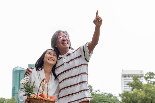 Pares mayores asiáticos con felicidad de la forma de vida de la cesta de fruta en parque.