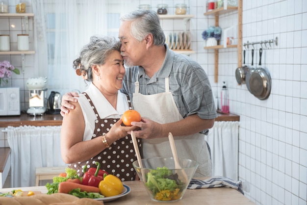 Pares mayores que se divierten en cocina con la comida sana - Jubilados que cocinan la comida en casa con el hombre y la mujer que preparan el almuerzo con las verduras bio - Concepto mayor feliz con el pensionista divertido maduro.