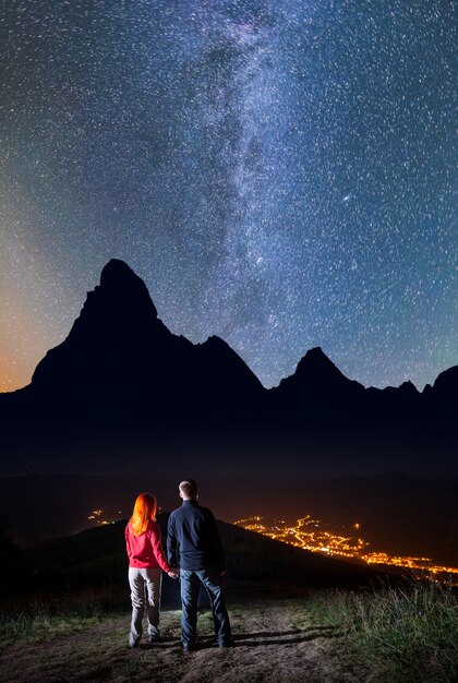 Pares românticos - menina e indivíduo que guardam as mãos, estando em um monte e apreciando o céu estrelado incredibly bonito na noite.