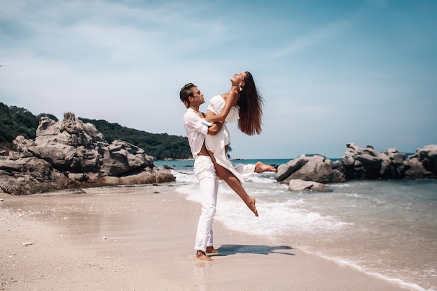 Pares românticos novos na roupa branca que beija em uma praia quente, tropical.