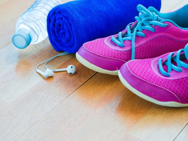 Pares de zapatos rosados ​​del deporte, toalla, botella de agua en piso de madera.