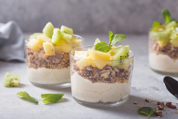 Parfait de iogurte caseiro com granola, kiwi, abacaxi e nozes em um copo no café da manhã saudável em fundo de concreto