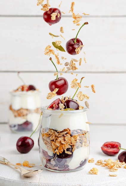 Foto parfait de granola con yogur griego y cerezas en madera blanca