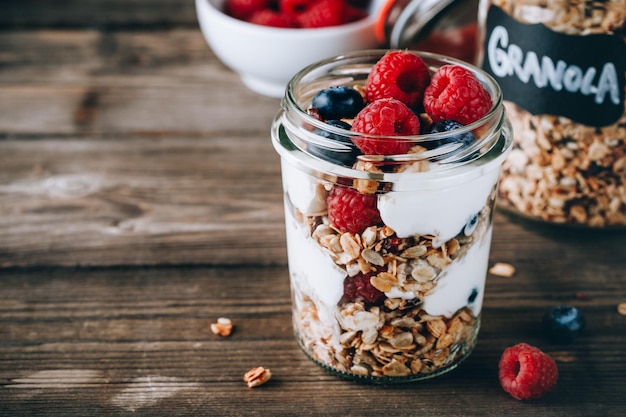 Parfait saludable de arándanos y frambuesas con yogur griego en tarro de vidrio sobre fondo de madera rústica