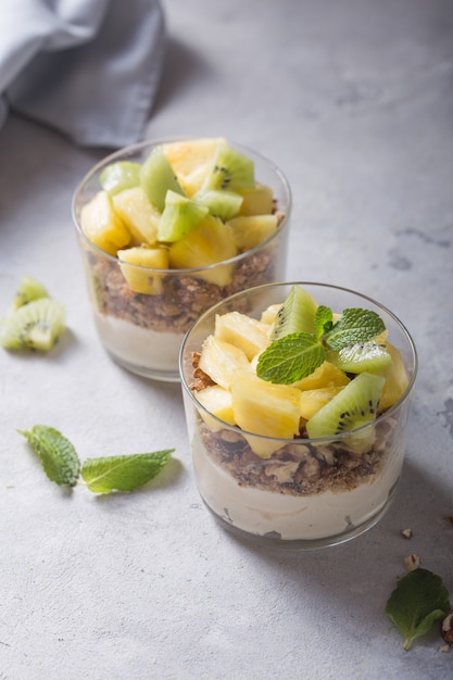 Parfait de yogurt casero con granola, kiwi, piña y nueces en un vaso para un desayuno saludable sobre fondo de hormigón