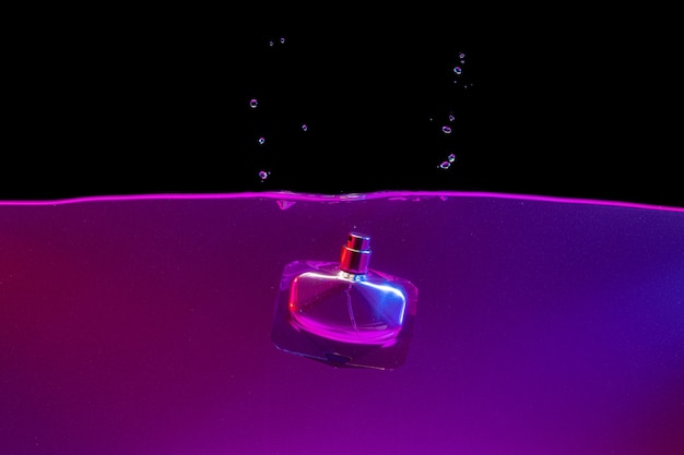 Parfümflasche, die mit einem Spritzer Neonlicht ins Wasser taucht