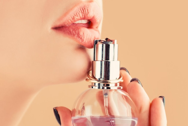 Parfümflasche für Frauen. Sexy Lippen. Rosa Lippe. Nahaufnahme sexy praller weicher Lippen mit dunkelrotem Lippenstift. Schönes Mädchen, das Parfüm verwendet. Frau mit Flasche Parfüm. Frau präsentiert Parfümduft