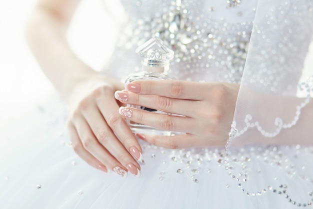 Parfümflasche in den Händen der Braut. Eine Frau bereitet sich auf ihre Hochzeit vor. Braut im eleganten Hochzeitskleid, schöne gepflegte Hände