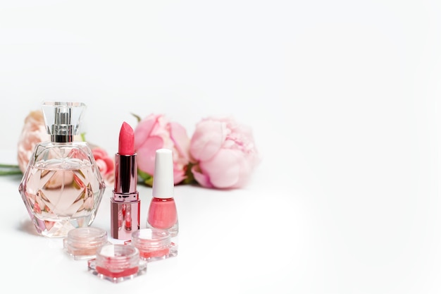 Parfümflasche, Nagellack, Lippenstift und Blumen auf weißer Oberfläche