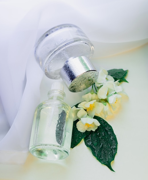 Parfümflaschen mit Wassertropfen und Jasminblüten Weißer Stoffhintergrund mit floraler Essenz