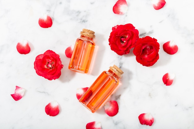 Parfümiertes Rosenwasser in Glasflasche und kleine rote Rosen mit Blütenblättern.