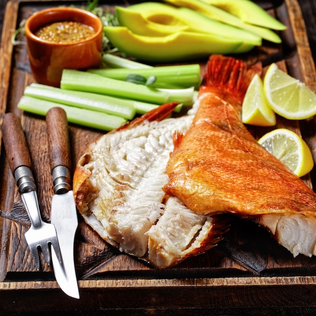 Pargo defumado a frio com talos de aipo, rodelas de limão, fatias de abacate e microgreens em uma bandeja de madeira rústica em uma mesa rústica, close-up