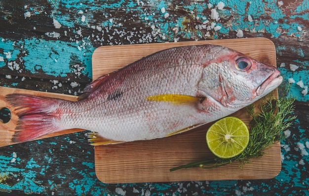 Pargo, preparado para cozinhar Contém limão e endro numa tábua de madeira.