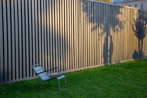 Parkstuhl und Schatten auf dem Parkzaun vom Sonnenuntergang im Septemberabendbäume und zwei Personen