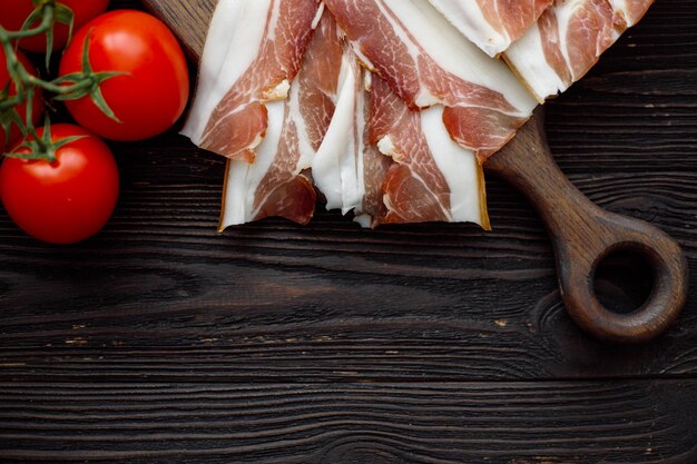 Parma-Schinkenscheiben auf dunklem Holzhintergrund mit flacher Lage der Tomaten-Draufsicht