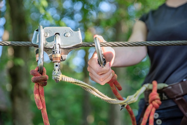 Parque de Aventuras Forestales. La mujer se abrocha el mosquetón y usa el equipo de escalada. Supera obstáculos en el parque forestal de aventuras. Banner para publicidad y lugar para insertar texto.