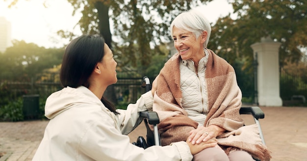 Parque de cadeiras de rodas e uma mulher idosa com uma deficiência falando com sua enfermeira durante uma caminhada ao ar livre Saúde médica e um cuidador feminino conversando com um paciente idoso ou residente em um jardim